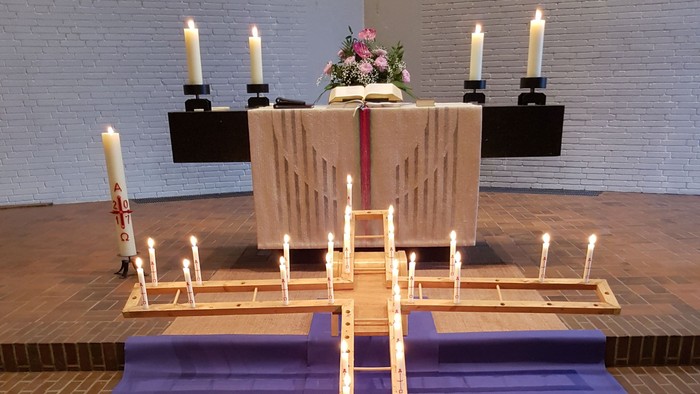 Ein Altar in einer Kirche mit brennenden Kerzen und Blumen.