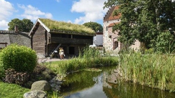 Charmerende historiske bygninger med græsklædte tage ved siden af en rolig, frodig vandvej.