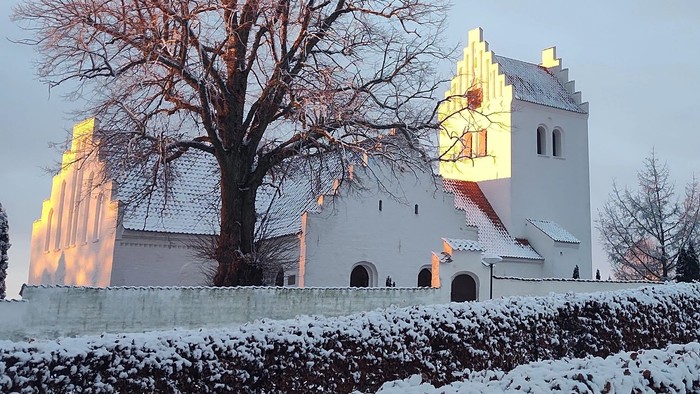 En snedækket kirke med en stor tårn og en træ i forgrunden