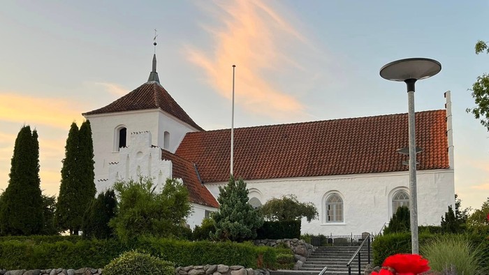 En hvid kirke med røde tagtag og en rød rose i forgrunden