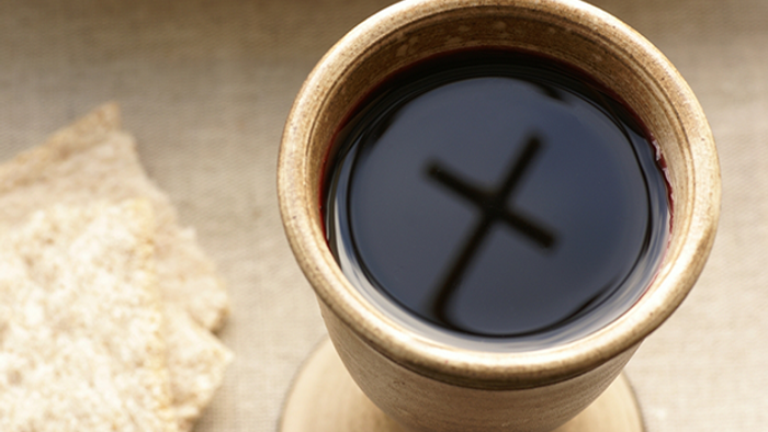 A glass of dark liquid with a cross reflection, beside a cracker.
