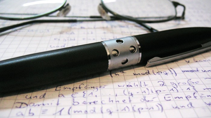 Ein schwarzer Stift und eine Brille liegen auf einem Notizblock mit mathematischen Notizen.