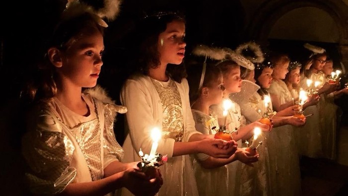 Children in white dresses holding candles, singing in a group.