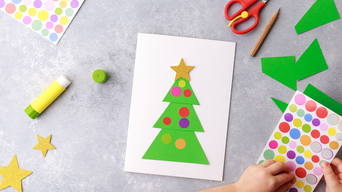 Kind bastelt einen Weihnachtsbaum aus Papier und Aufklebern.