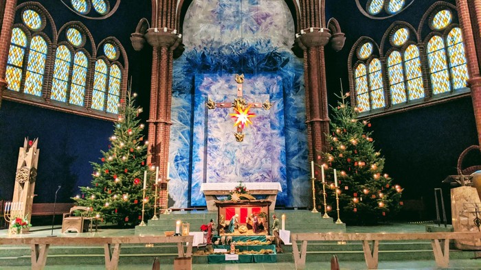In der Kirche stehen zwei Weihnachtsbäume vor einem Altar mit Kreuz.
