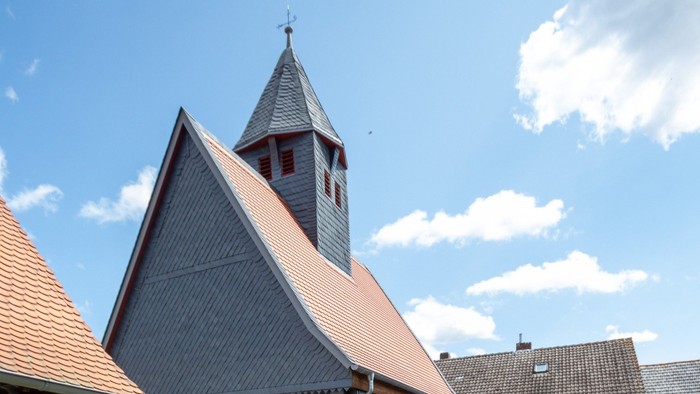 Graues Haus mit rotem Dach und Glockenturm unter blauem Himmel.