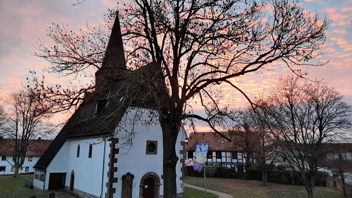 Kirche mit Turmspitze und kahlen Bäumen bei Sonnenuntergang