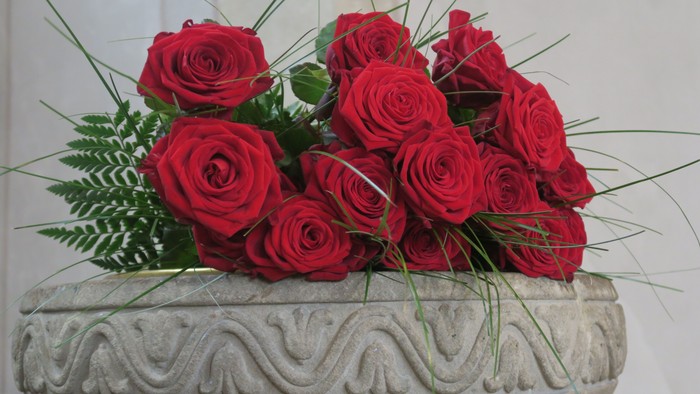 Hier sieht man den oberen Rand des Taufsteins in der Johanneskirche mit Ornamenten. Darauf liegen einige rote Rosen.
