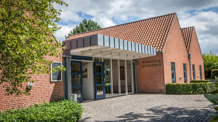 Et rødt teglsteinshus med skråt tag og en indgang med glaspaneler.