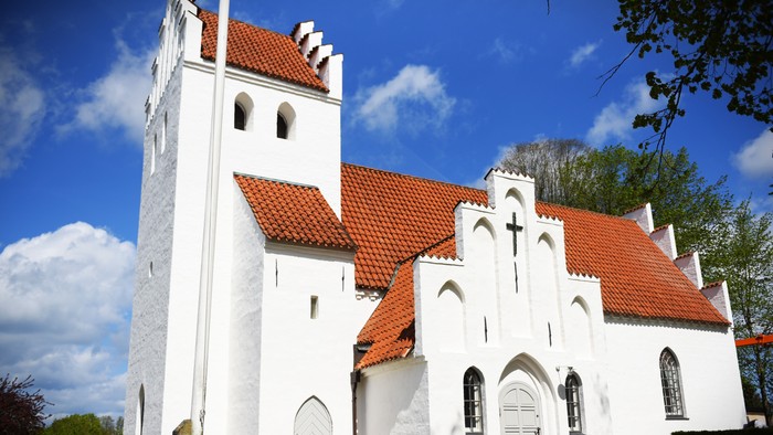 Et hvidt kirkebygning med røde tag og tårn mod en blå himmel