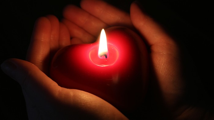Sanfte Hände halten eine brennende rote Kerze und erzeugen ein warmes Leuchten.