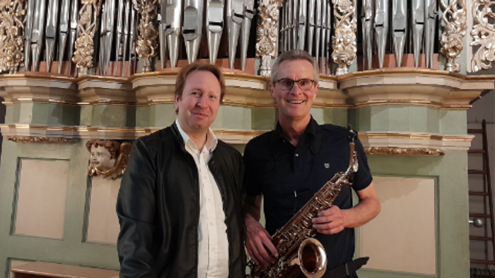 Zwei Männer posieren mit einem Saxophon vor einer prächtigen Orgel.