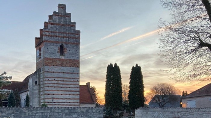 En juletree foran en kirke med klokketårn og islagede græsflader