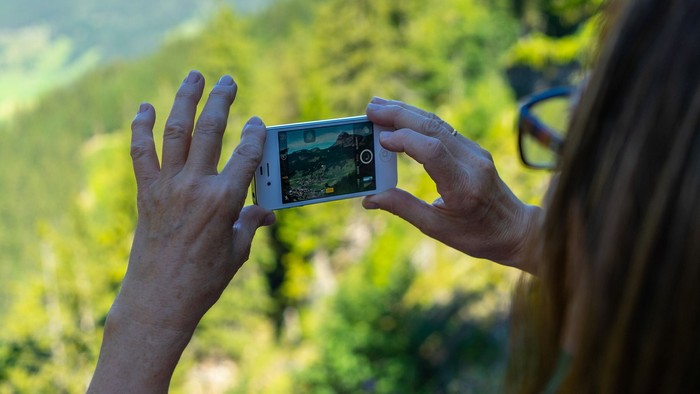 Eine Person hält ein Smartphone und macht ein Foto von einer grünen Landschaft.