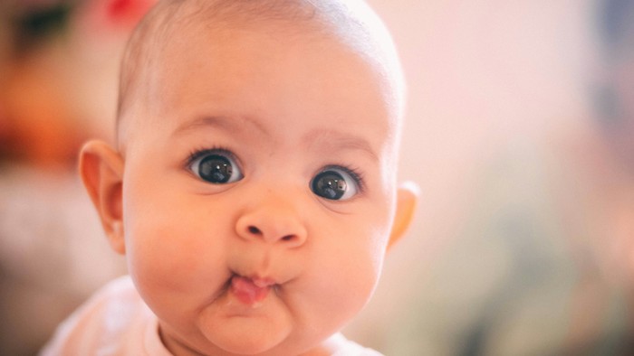 Et spæd barn med store blå øjne og en rosa klæde.