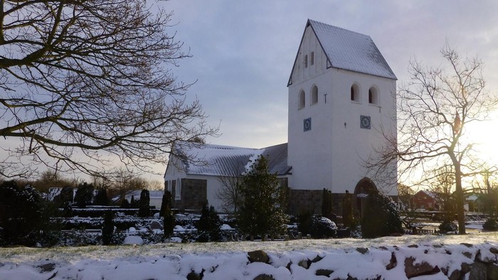 En snede kirke med tårn og nøgler i vinduerne, omgivet af sne og nakke træer