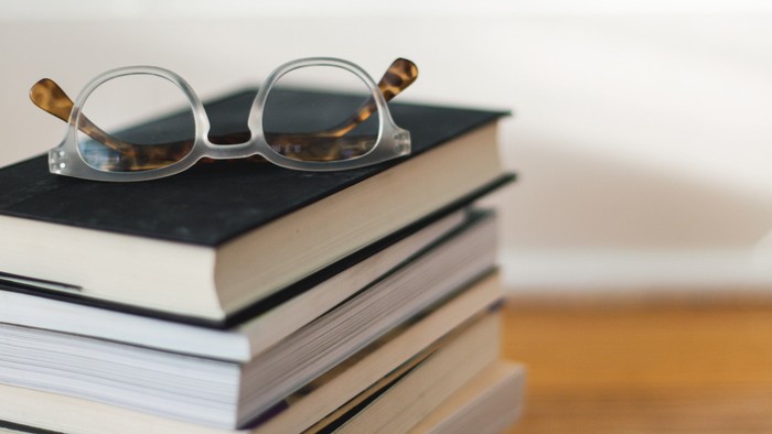 Bücherstapel auf einer Tischplatte, darauf eine Brille