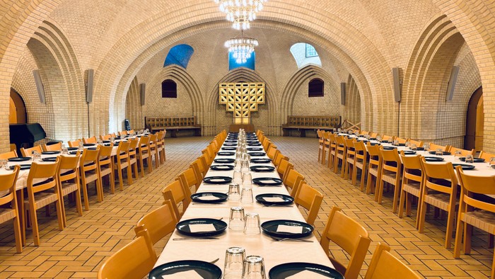 Stor underjordisk spisesal med lang bord, belysning og høje vægge