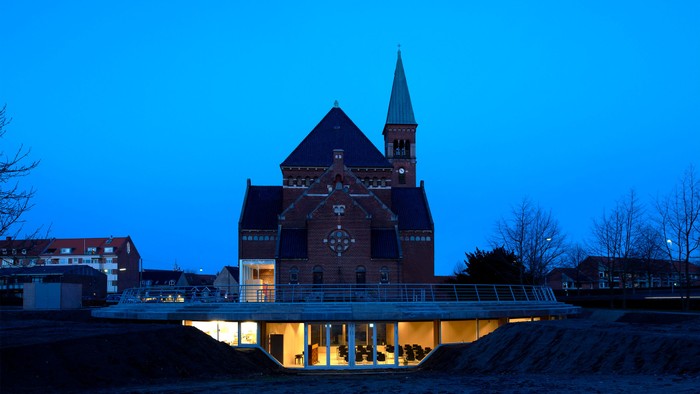 En belyset bro forløber foran et stort, mørkt kirkebygning med to spire.