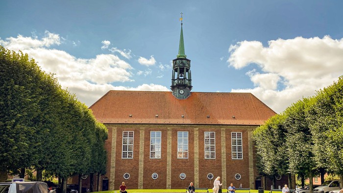 Stort murstensbygning med urtårn og mennesker, der går rundt.