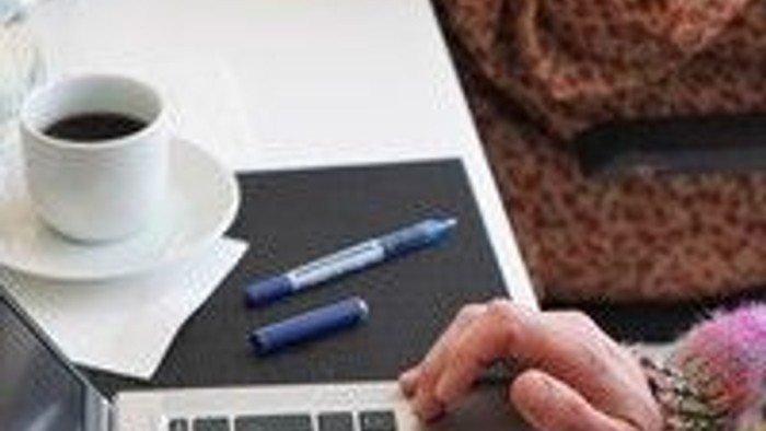 En person arbejder på en laptop ved et bord med en kaffe og en pen.