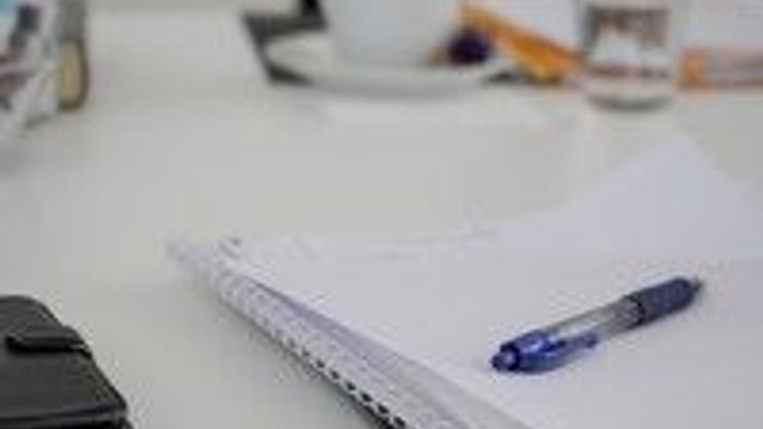 En skrivebord med papir, pen og en telefon.