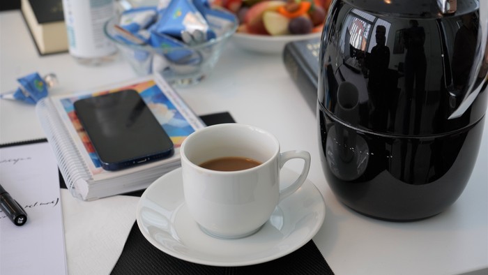 En skrivebord med kaffe, mobiltelefon, notatblok og frugter