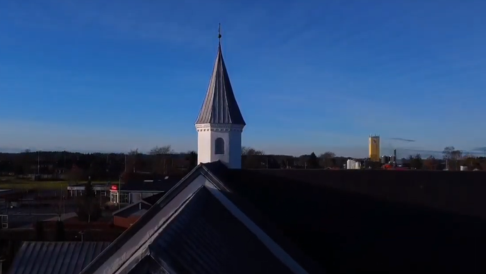 En hvid kirke med spir og en sort tak mod et blåt himmel.