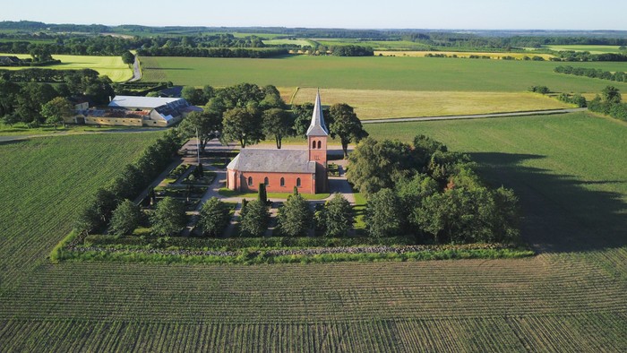 En rød kirke i en grøn dal med jordbrugslandskab