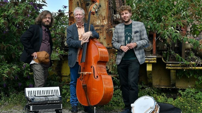 Drei Männer posieren mit Musikinstrumenten im Freien.