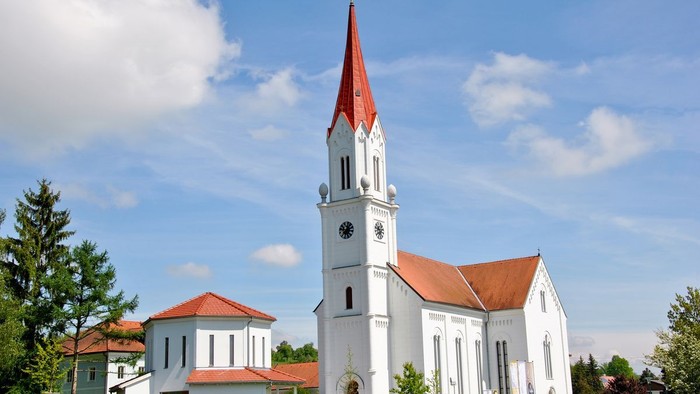Weiße Kirche mit hohem Turm und rotem Dach vor blauem Himmel