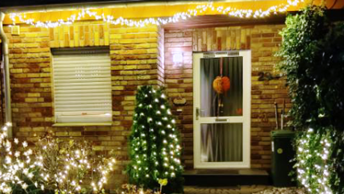 Ein festlich geschmücktes Haus mit Lichtern und einem kleinen Weihnachtsbaum.