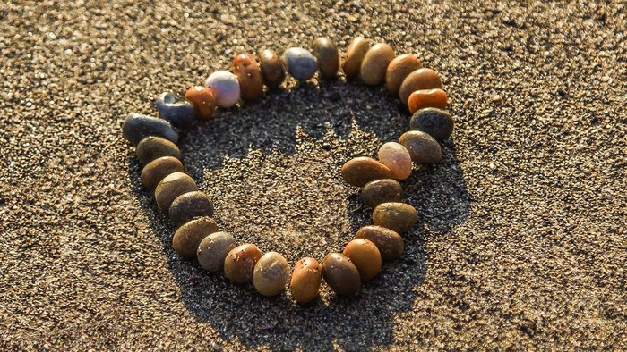 Ein Armband aus Perlen liegt auf sandigem Boden.