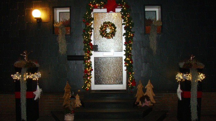 Weihnachtsdekorationen umgeben nachts eine Haustür.