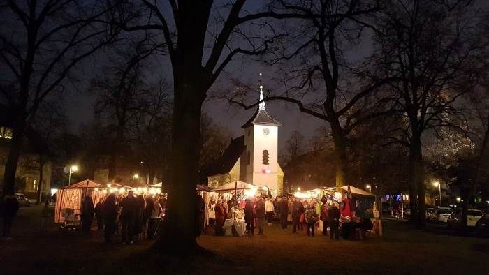 Nächtlicher Weihnachtsmarkt vor Kirche mit vielen Besuchern