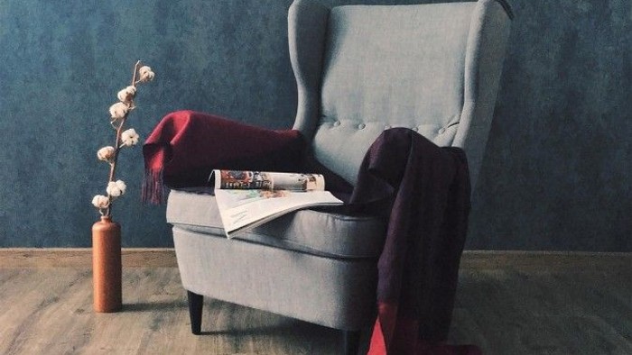 Gemütliche Leseecke mit blauem Sessel, Zeitschrift und Vase mit Baumwollzweigen.