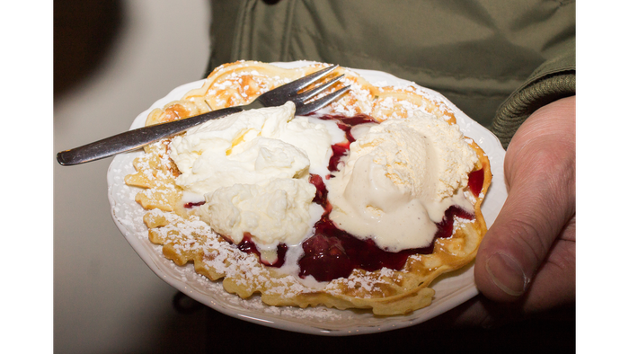 Hand hält Teller mit Pfannkuchen, Sahne und Kirschsoße