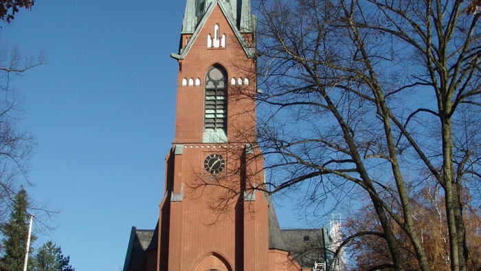 Große rote Kirche mit hohem Turm und grünem Dach in Parkanlage