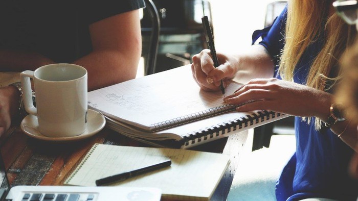 En gruppe af mennesker sidder ved et bord med laptopter, noter og kaffe.