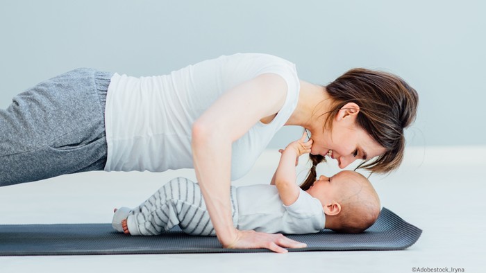Eine Frau übt Yoga mit ihrem Baby auf einer Matte.