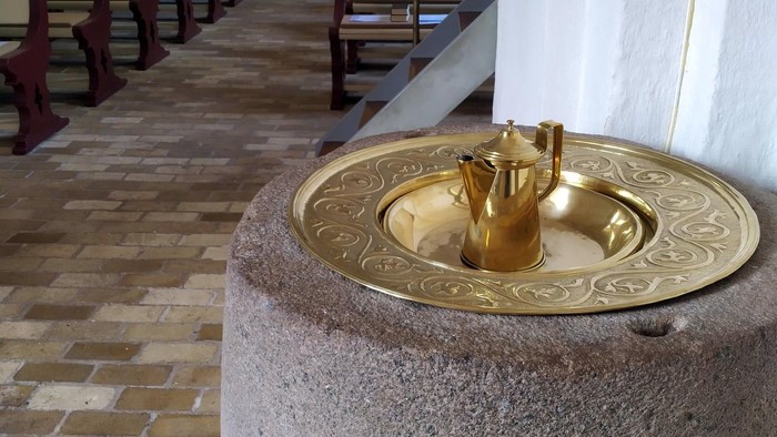 En kirke med stenfontæne og træbænke.