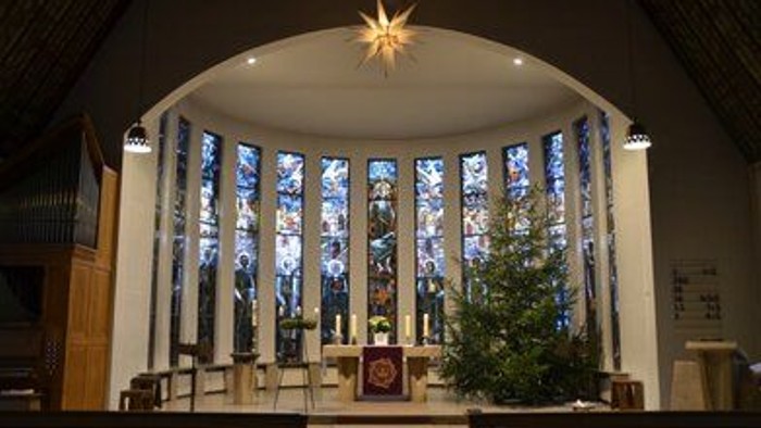 In der Kirche steht ein geschmückter Weihnachtsbaum vor einem großen Fenster.