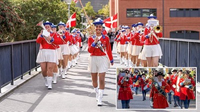 Marchingband i røde og hvide uniformer, der bærer flag og spiller på instrumenter.