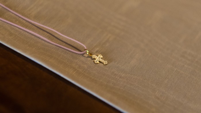 Ein kleines Goldkreuz an einem Faden liegt auf einer textilen Unterlage.