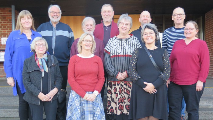 En gruppe af 11 personer står sammen på trin til et bygning