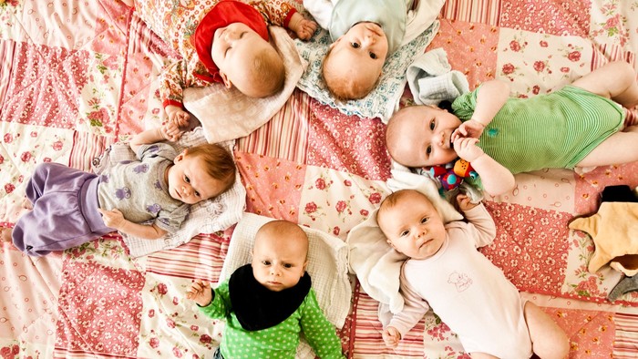 Syv spædende børn ligger på en rosa og hvid patchworkede dekke