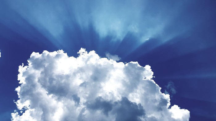 Strahlende Sonnenstrahlen erleuchten eine riesige, flauschige Wolke vor einem tiefblauen Himmel.
