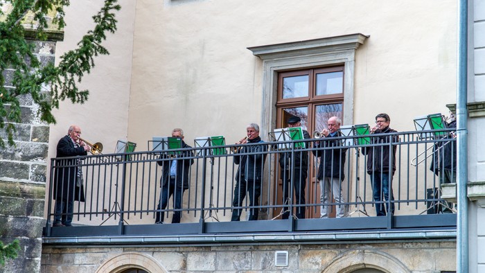 Ein Chor singt auf einem Balkon vor einem Gebäude.
