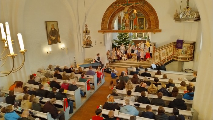 Blick von der Empore in die gefüllte St. Petri-Kirche in Rieseby. In den Bänken sitzen Menschen in Wintermänteln, im Altarraum sitzen und stehen die Krippenspielkinder.
