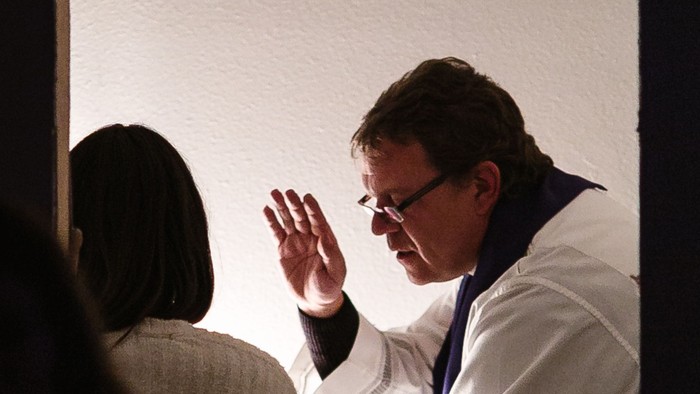 Ein Mann in weißem Anzug winkt auf einer Bühne.